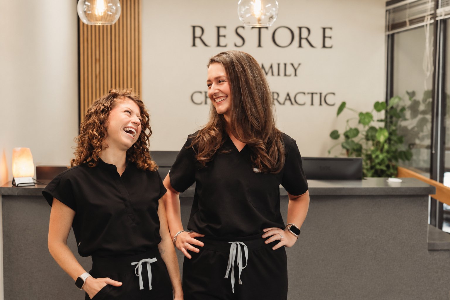 Dr. Lauren Rissman and Dr. Morgan Jones laughing together at the Restore Family Chiropractic front desk